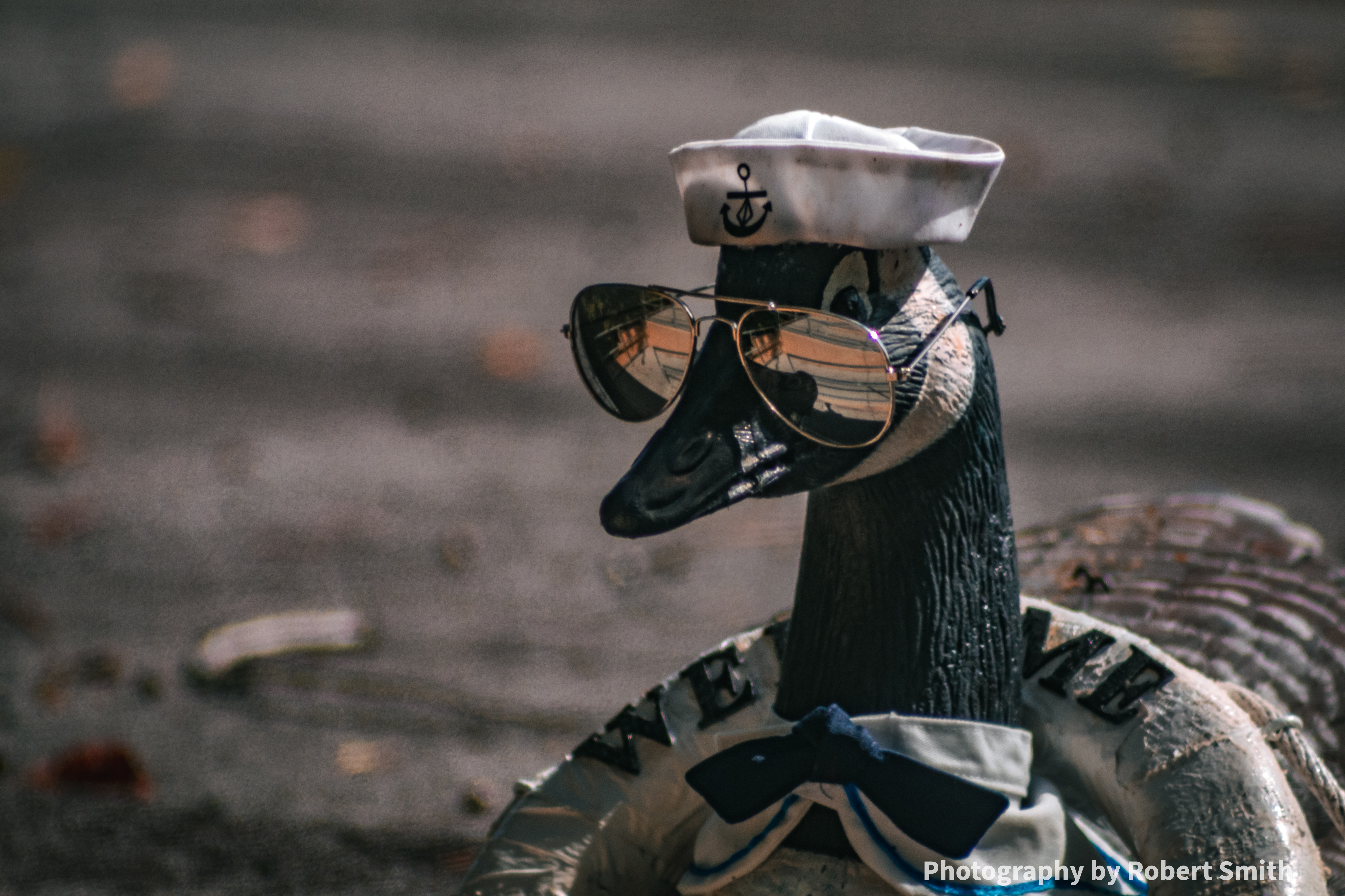 Close-up of a goose statue wearing mirrored aviator sunglasses and a white cap with an anchor emblem.
