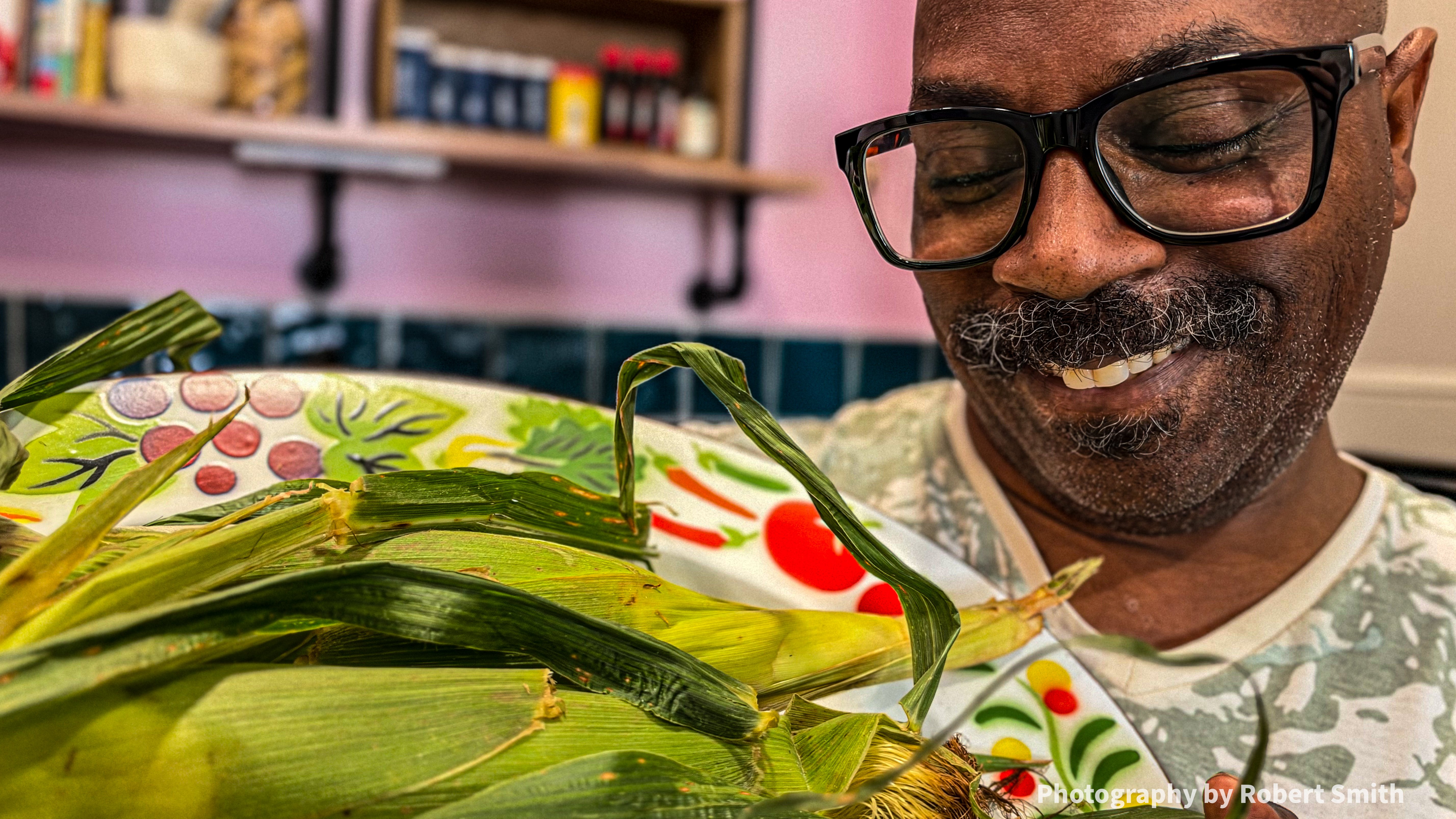 A close view shows Robert smiling down at the platter and ears of corn near his face.
